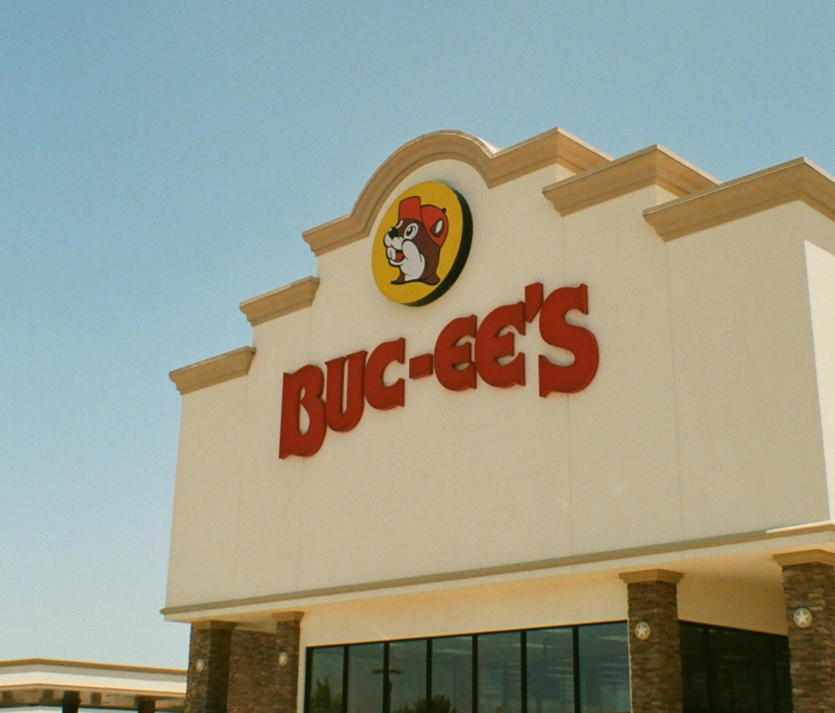 Exterior view of a Buc-ee’s travel center featuring the red “Buc-ee’s” sign and beaver logo on the building facade against a clear sky.