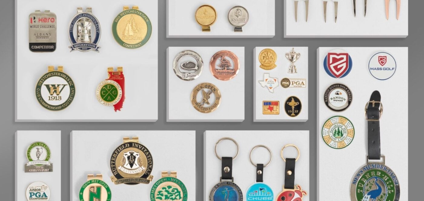 Display of custom golf event merchandise including metal bag tags, ball markers, keychains, lapel pins, and belt-style bag tags featuring various tournament and club logos.