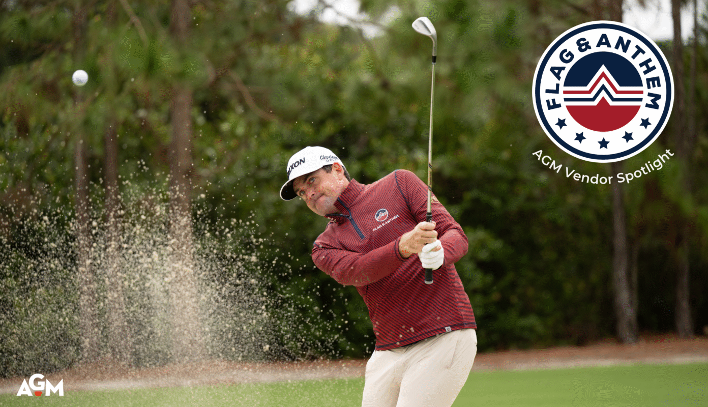 Golfer hits a shot from a sand bunker with sand flying mid-air, wearing a red-striped Flag & Anthem quarter-zip pullover, white Srixon hat, and white gloves, with the Flag & Anthem and AGM Vendor Spotlight logos displayed in the top right corner.
