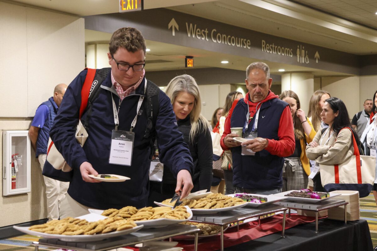 Conference attendees line up at a refreshment table featuring a variety of cookies and brownies during a break.