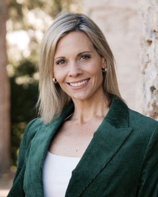 Tracy Stearns headshot. Blond-haired woman in a white top and green blazer smiling into the camera.
