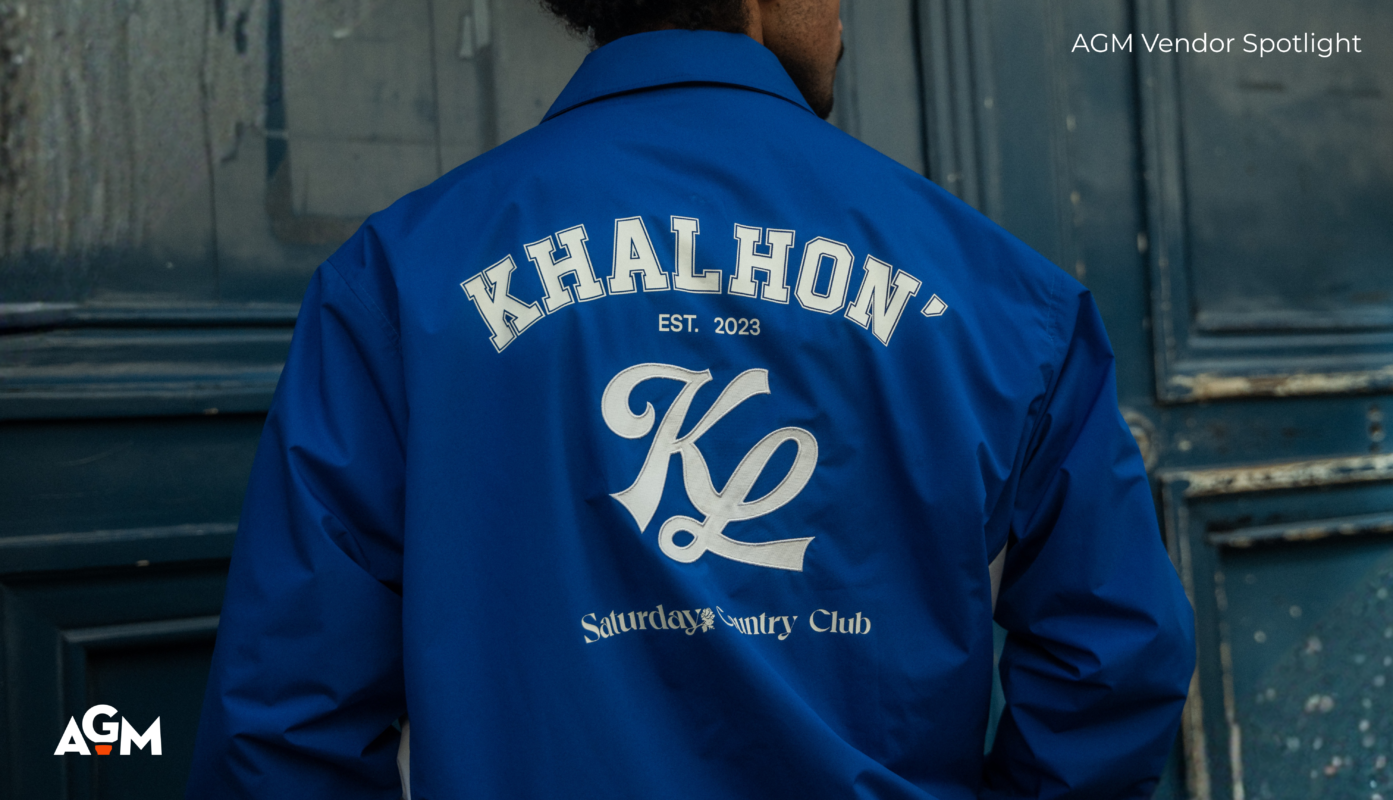 Back view of a model wearing a royal blue Khalhon jacket with large embroidered branding reading “Khalhon Est. 2023,” “KL,” and “Saturday Country Club,” photographed against a weathered blue door with AGM Vendor Spotlight text overlay.