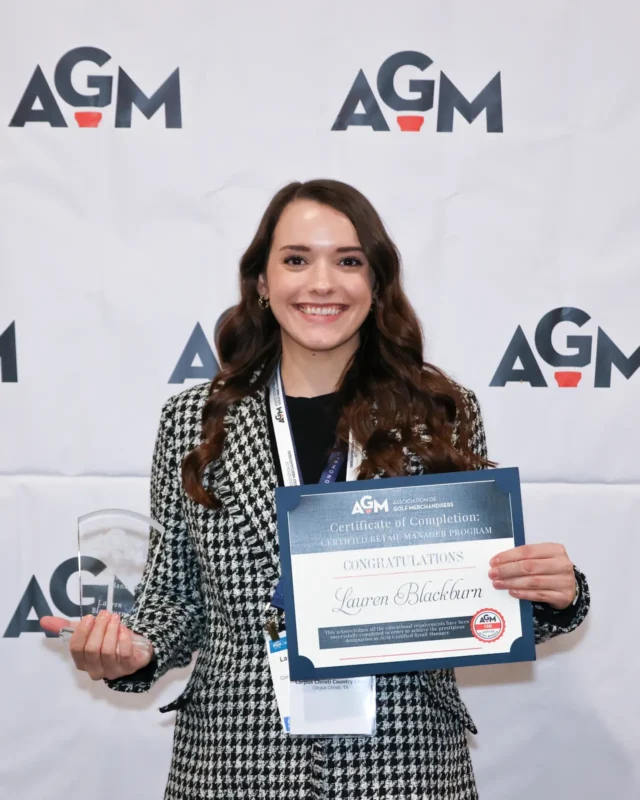 Lauren Blackburn, Certified Retail Manager (CRM), holding her AGM Certificate of Completion and crystal award in front of an Association of Golf Merchandisers branded backdrop.