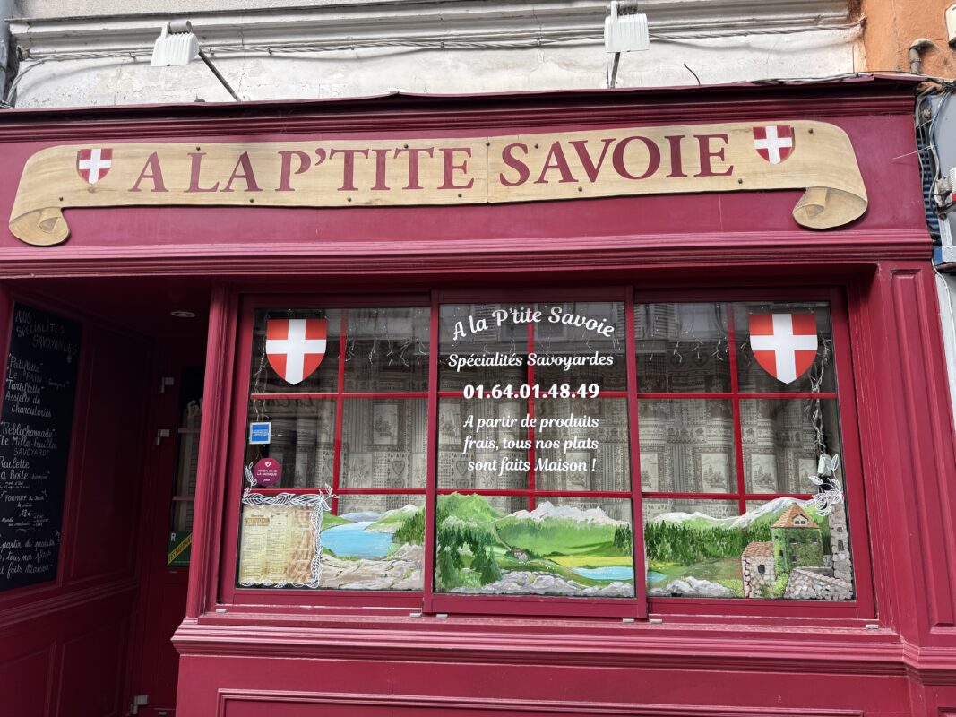 French storefront window featuring a window painting of a Swiss mountainous landscape.