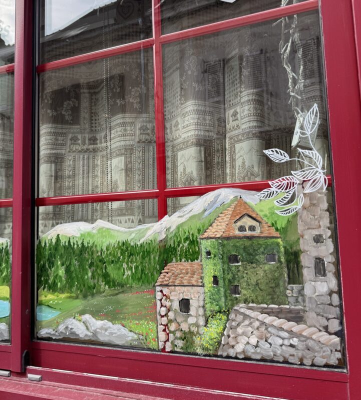 French storefront window featuring a window painting of a Swiss mountainous landscape.
