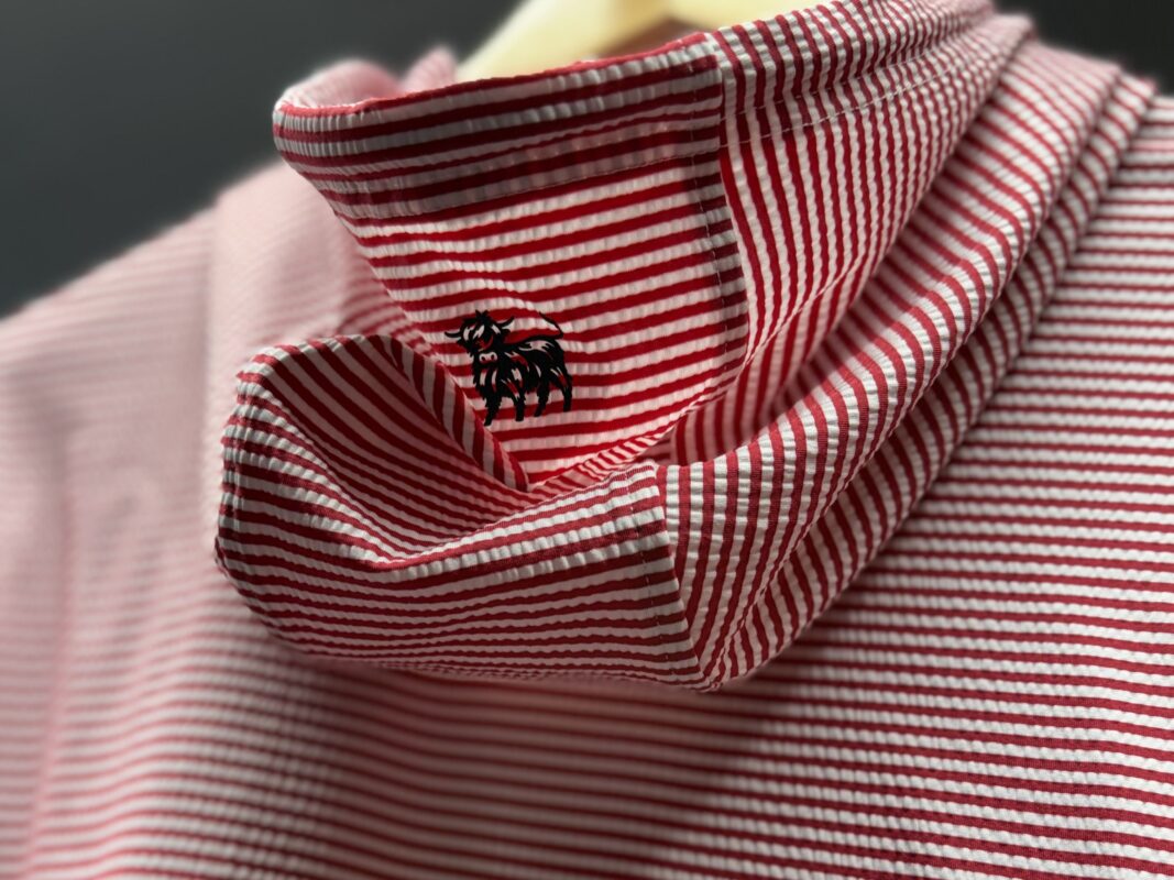 Red and white striped seersucker hoodie hanging on a wooden hanger, featuring a structured collar embroidered with the Zipelly logo.