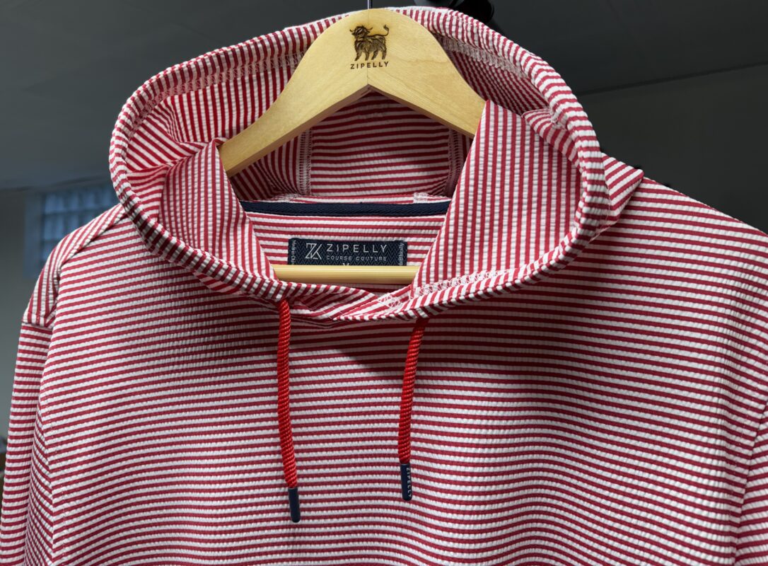 Red and white striped seersucker hoodie hanging on a wooden hanger engraved with the Zipelly logo, featuring a structured collar, red drawstrings with dark tips, and visible interior branding at the neckline.