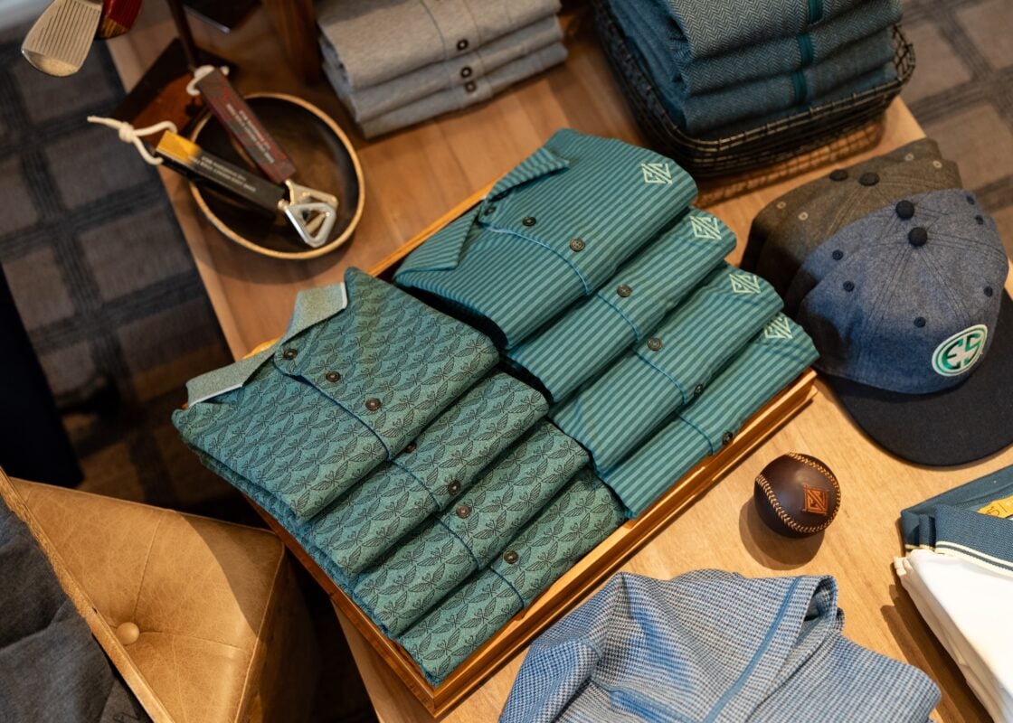 Overhead view of a golf lifestyle retail display at Interlachen Country Club featuring coordinated stacks of technical knit polos, branded headwear, and Field Day themed accessories.