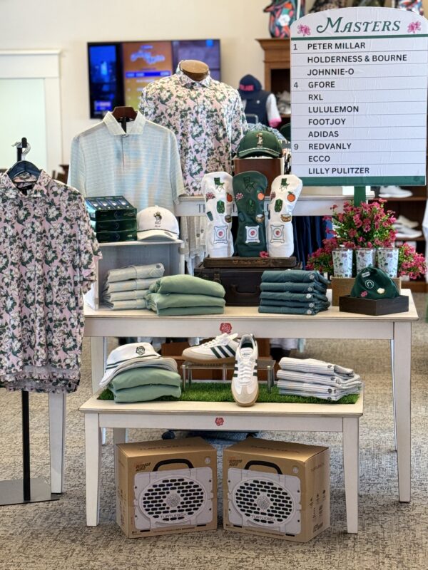 Golf shop display featuring Masters-themed merchandise with green apparel, floral prints, accessories, and leaderboard-style signage