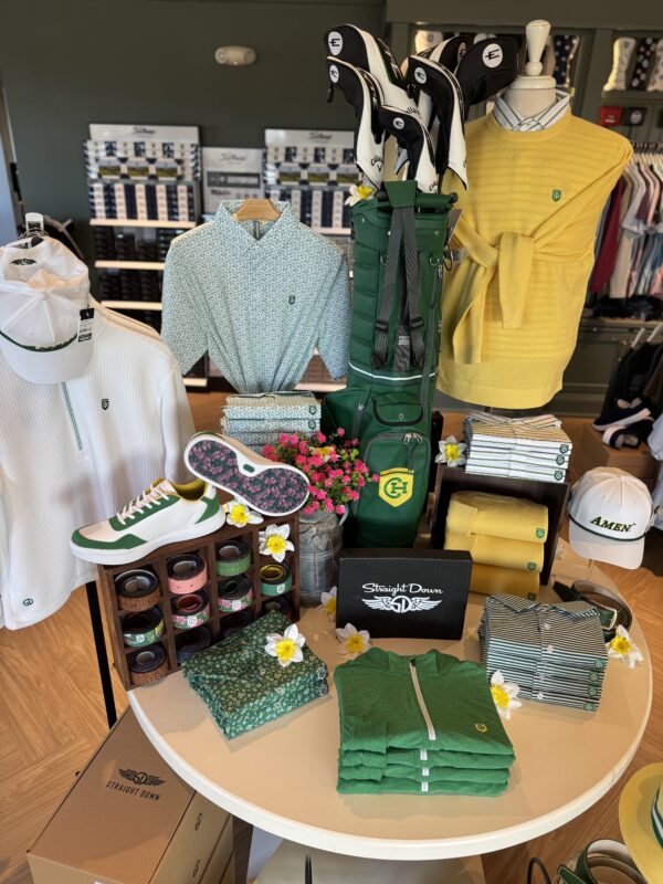 Golf shop display featuring green and yellow apparel, floral accents, accessories, and a golf bag styled for a Masters-inspired theme