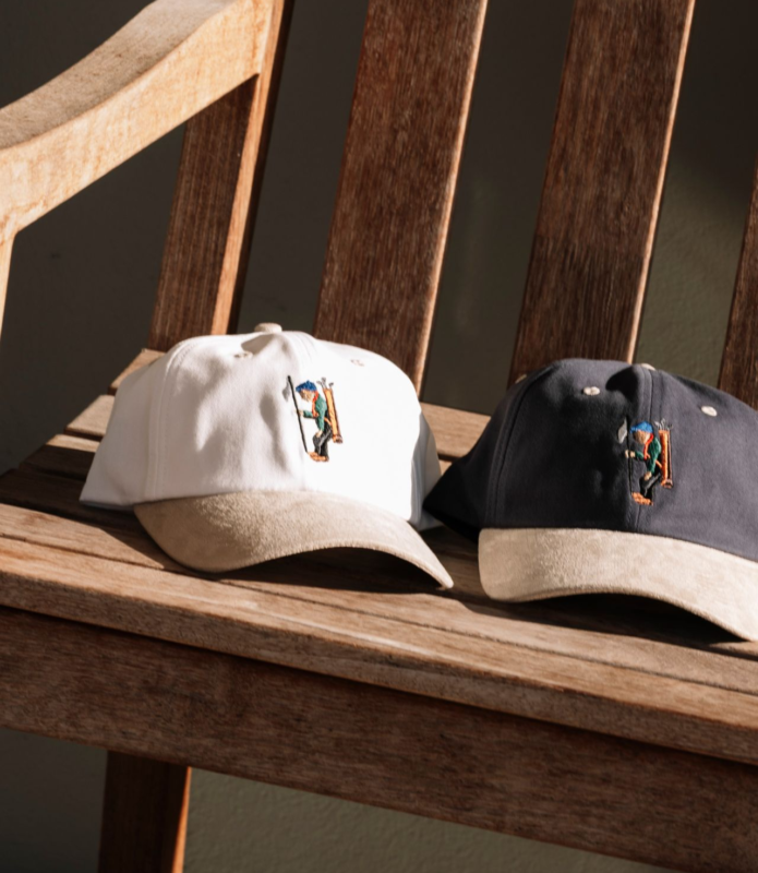 Two golf caps with embroidered golfer designs rest on a wooden bench, one white and one dark navy, both with light-colored suede-style brims.