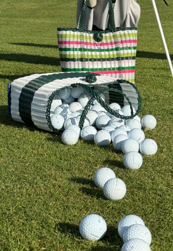 Woven tote and cylindrical bag on a golf course with golf balls spilling out onto the grass, showing green, white, and pink striped design