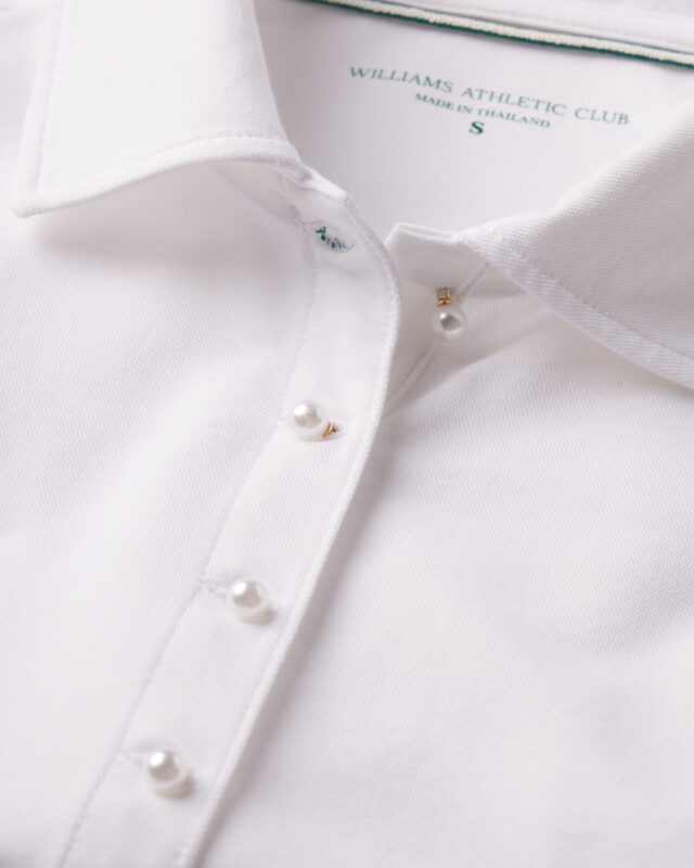 Close-up of a white textured polo shirt with pearl buttons and gold accents, featuring a Williams Athletic Club label inside the collar.