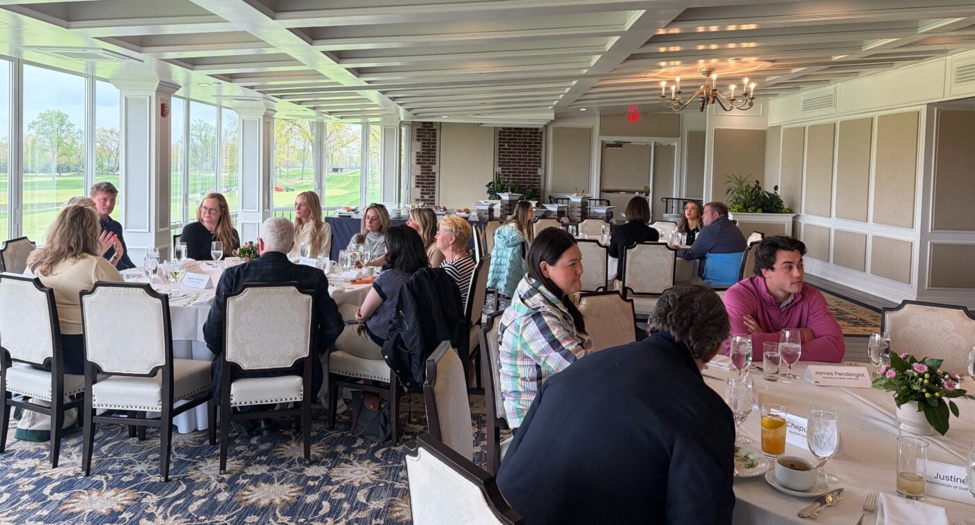 AGM members and golf industry professionals seated at round tables during a regional networking and discussion event inside a bright clubhouse dining room overlooking the golf course.