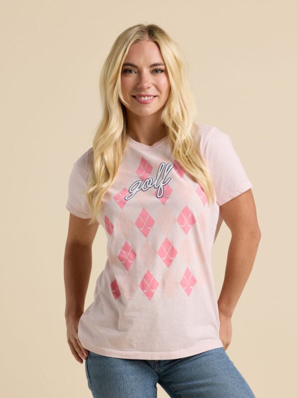 Woman wearing pale pink golf-themed T-shirt with pink argyle pattern, crossed golf clubs, and blue cursive “golf” lettering.