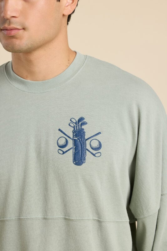 Close-up of sage green sweatshirt chest embroidery featuring a golf bag with crossed clubs and golf balls.