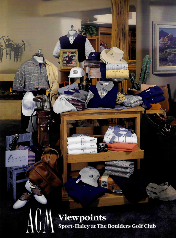 Golf shop merchandising display featuring coordinated apparel and accessories arranged on tiered wooden tables and display fixtures. The presentation includes patterned golf polos, sweater vests, folded knitwear, hats, golf shoes, leather bags, golf clubs, and branded accessories in shades of navy, gray, cream, and burgundy. Decorative elements such as framed photography, western-style hats, cacti, and rustic wood accents create a sophisticated Southwestern-inspired lifestyle display that highlights color coordination and layered visual merchandising. Visible branding throughout the display includes the name “Sport Haley” on apparel and signage.