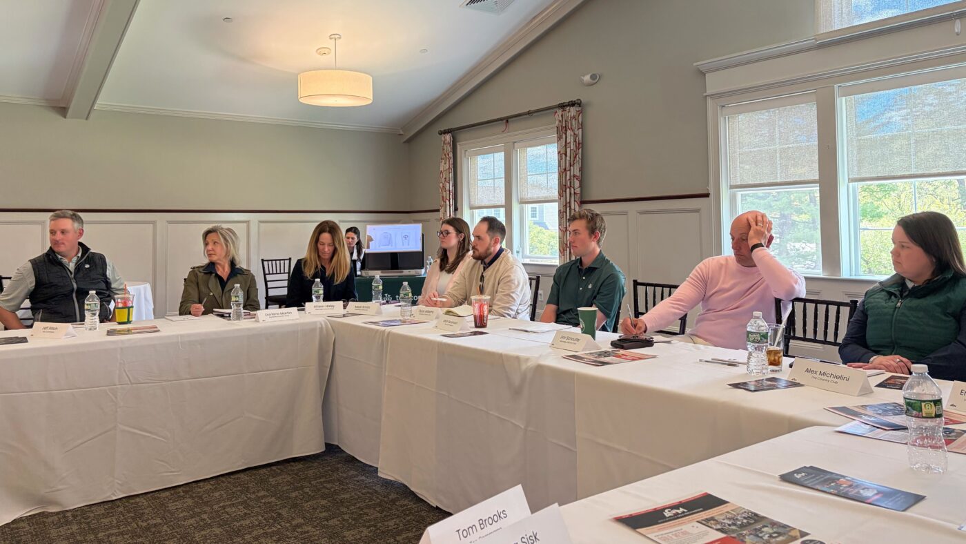Attendees seated around U-shaped conference tables participate in a discussion during an AGM regional educational session, taking notes and engaging with fellow golf retail professionals.