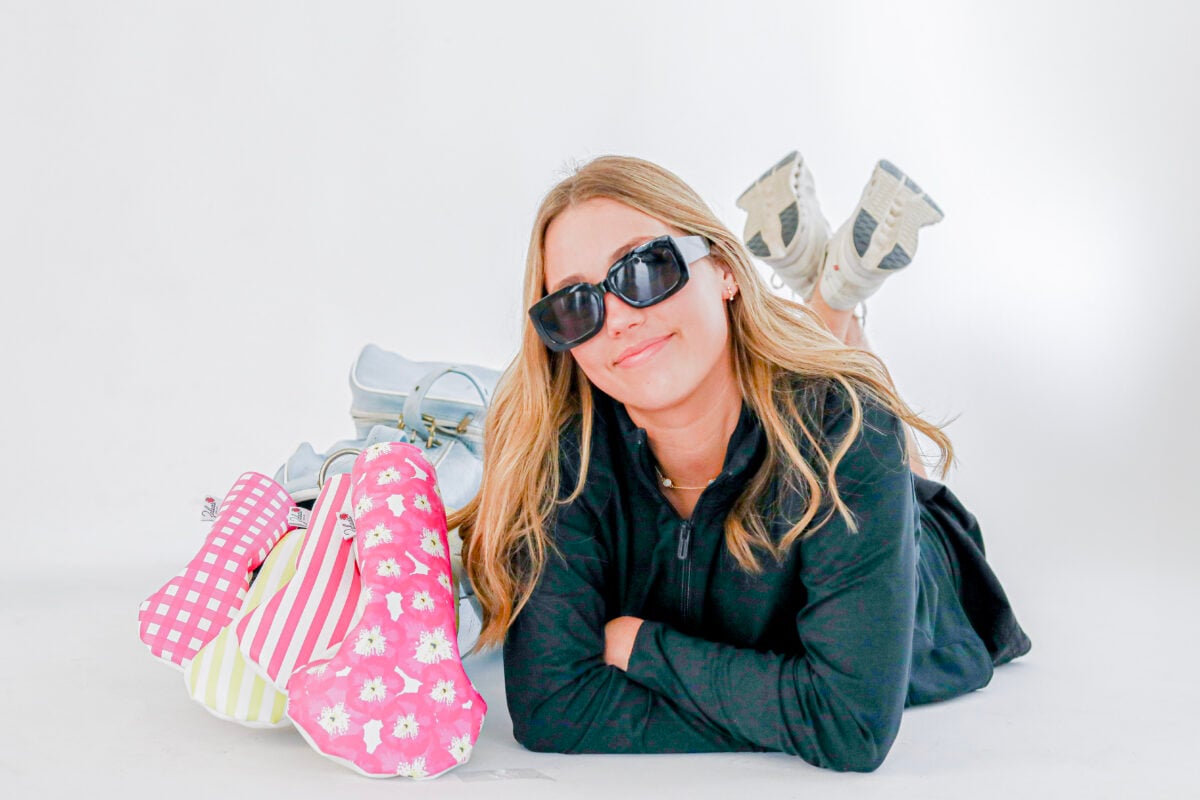 Woman in sunglasses posing on the ground beside colorful golf headcovers from Zalea's Golf Co.