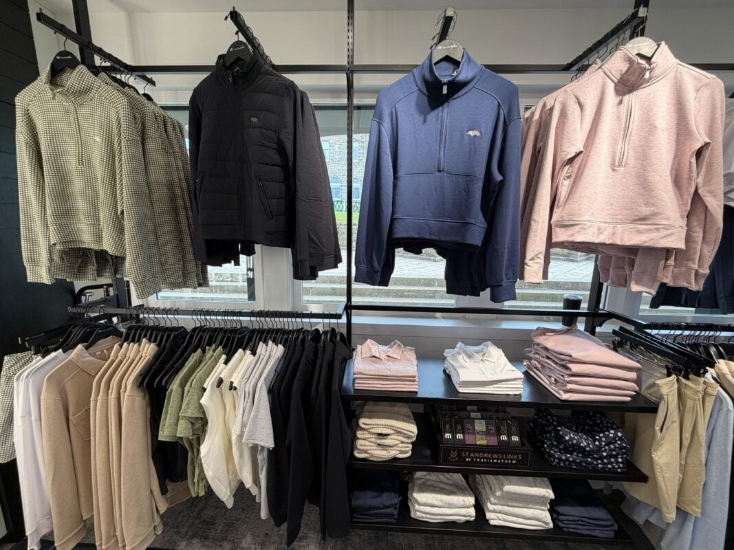 Photo of a St Andrews Links golf shop apparel display featuring jackets, quarter-zips, polos, and folded clothing in neutral, blue, and pink tones.