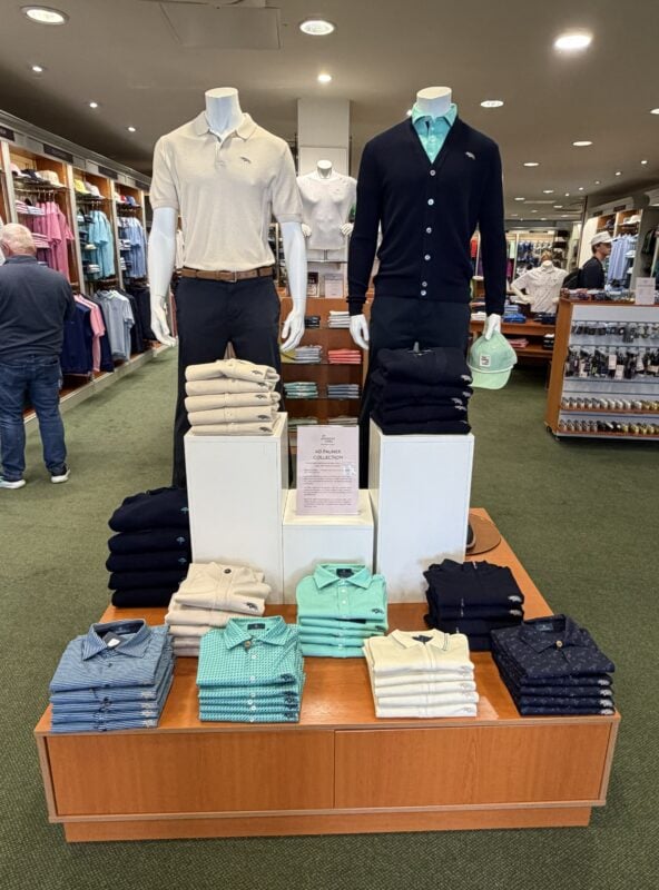 Photo of an Arnold Palmer Collection display inside The Old Course Shop, featuring mannequins and neatly folded polos, sweaters, and cardigans in navy, cream, and aqua.