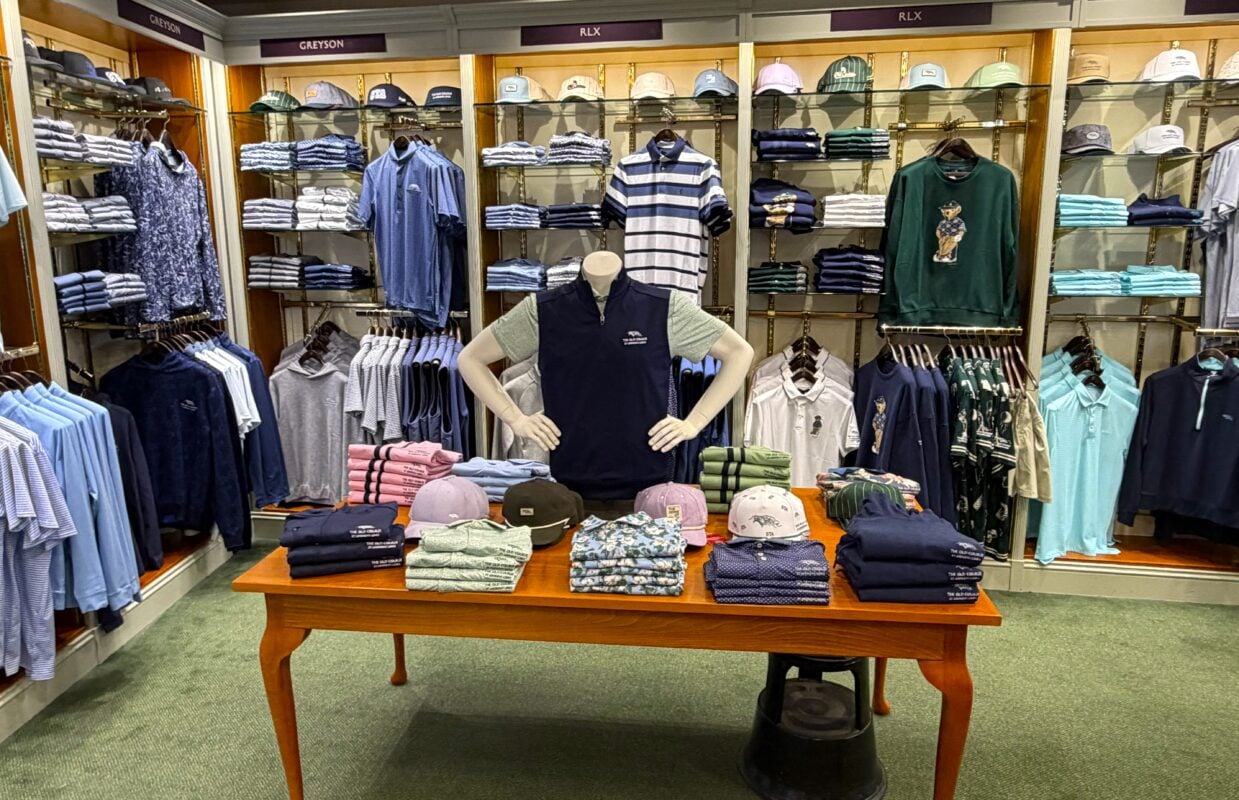 Photo of a men’s apparel display inside The Old Course Shop, featuring neatly arranged polos, hats, sweaters, and outerwear from Greyson and RLX.