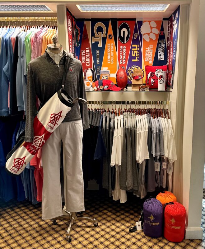 College football-themed golf shop display featuring a mannequin in club apparel, golf bag, and pennants for South Carolina, Georgia Tech, Tennessee, Georgia, LSU, Clemson, Mississippi, and Kentucky, with team accessories and a football.