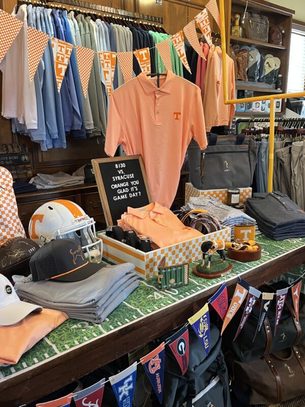University of Tennessee football-themed golf shop display featuring orange apparel, a Tennessee helmet, pennant banners, hats, accessories, and a sign reading “8/30 vs. Syracuse, Orange You Glad It’s Game Day?”