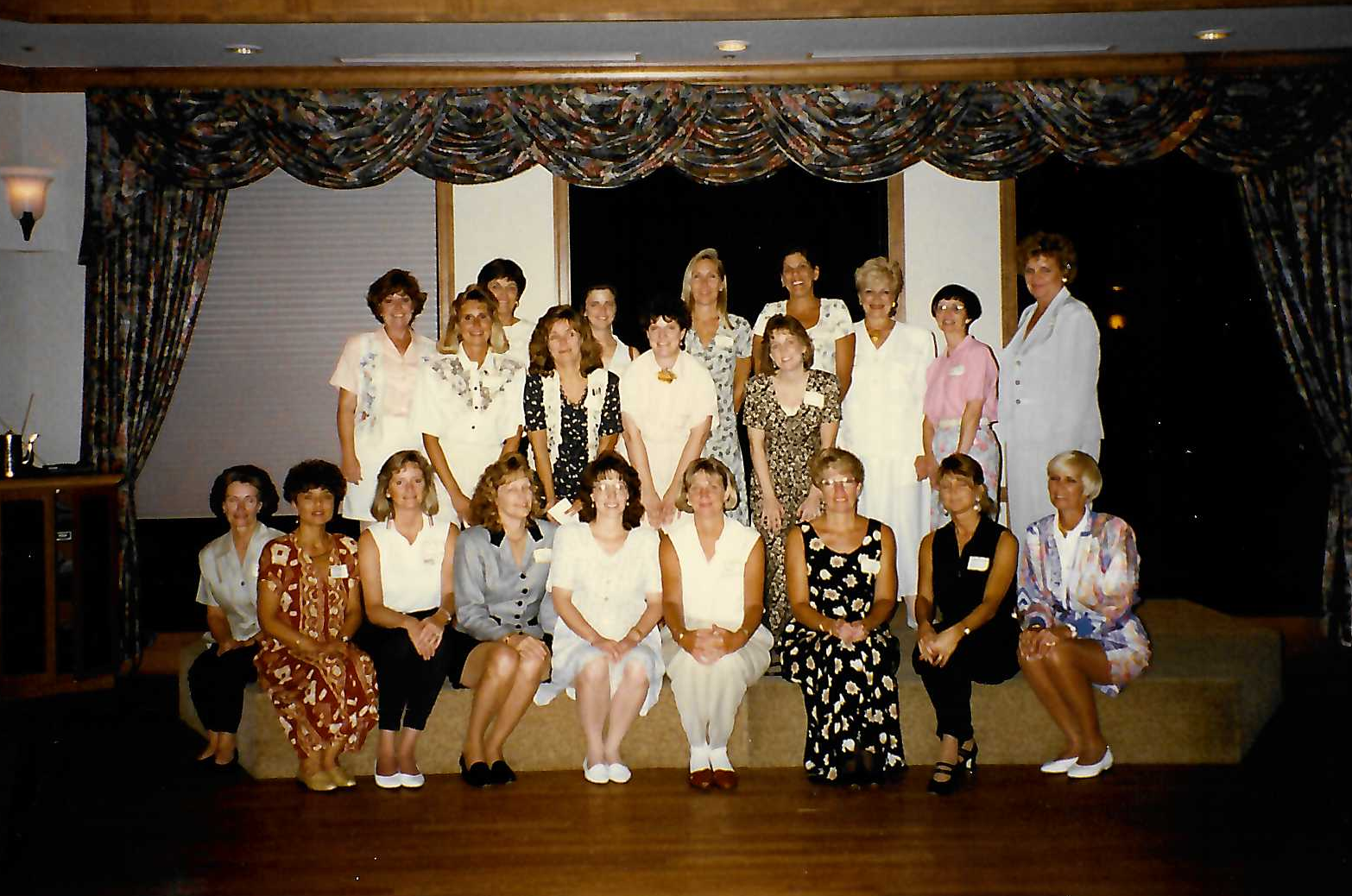 Historical group photo of approximately 20 women posing together in two rows at an indoor gathering, dressed in business and casual attire.