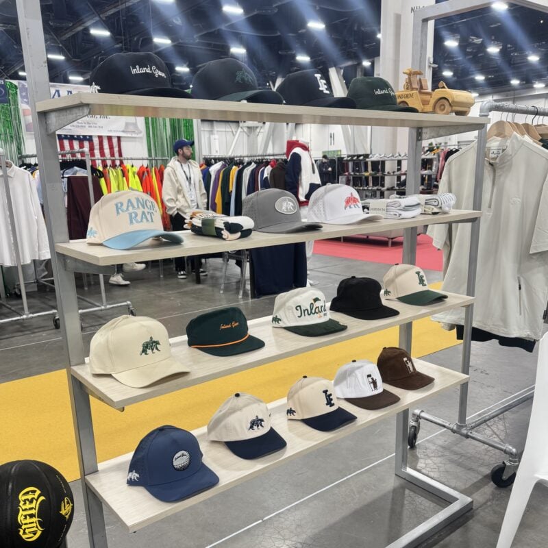 Photo of golf hats and folded apparel displayed on a multi-level shelf at a retail trade show.
