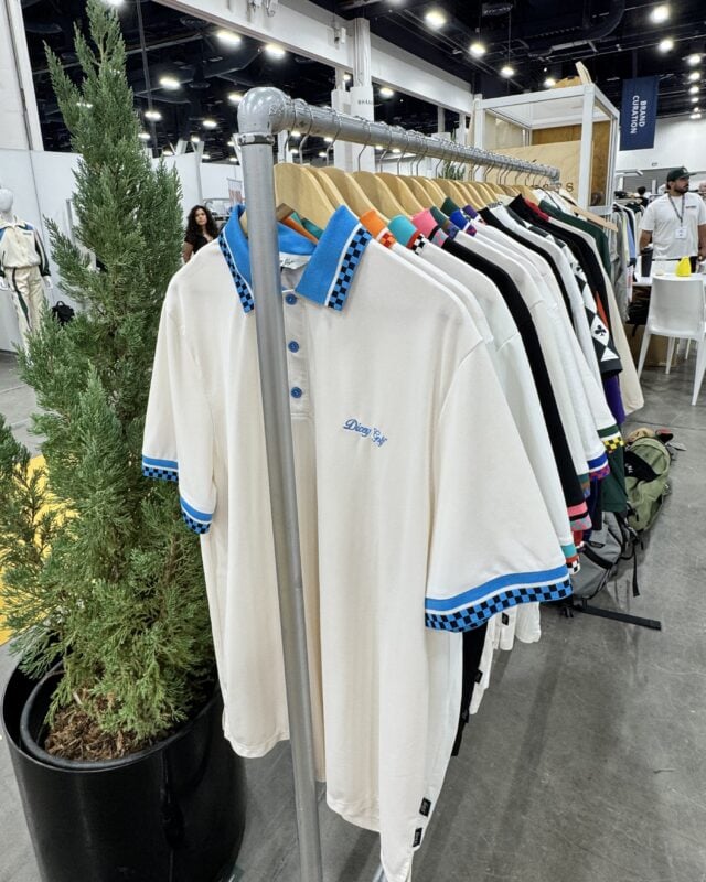 Photo of colorful golf polos displayed on a clothing rack at a golf retail trade show, featuring contrasting patterned collars and sleeve details.