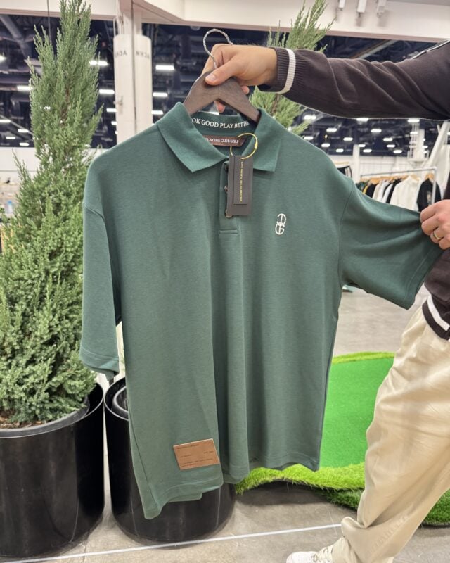 Photo of a forest green golf polo being displayed on a hanger at a golf retail trade show, featuring an embroidered chest logo and branded details.