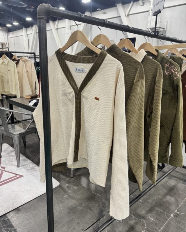 Photo of textured cream and olive green long-sleeve apparel displayed on a clothing rack at a retail trade show.