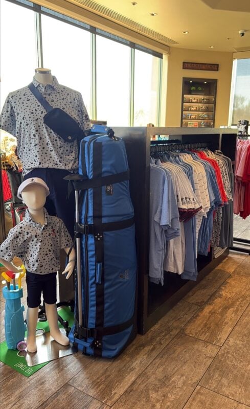 Golf shop display featuring adult and child mannequins in matching patterned polos beside a blue golf travel bag and coordinated apparel.