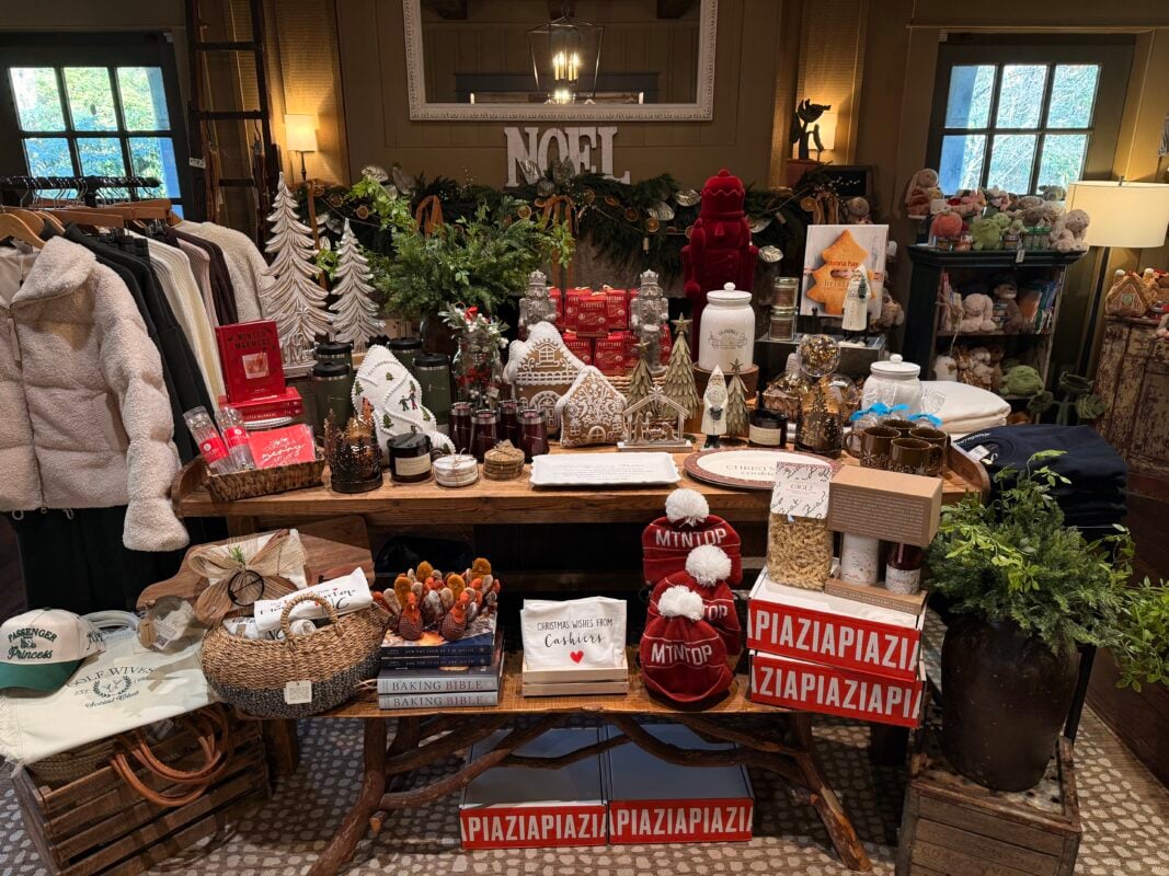Christmas retail display at Mountaintop Golf and Lake Club featuring gingerbread houses, miniature trees, holiday decorations, seasonal gifts, apparel, books, and gourmet treats arranged on rustic wooden tables beneath a festive NOEL sign.