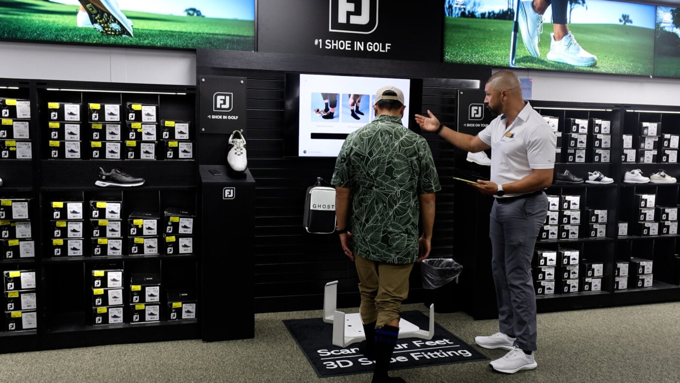 Photo of a customer using a Volumental 3D foot scanner for a golf shoe fitting at Haggin Oaks, assisted by a staff member in the FootJoy footwear section.