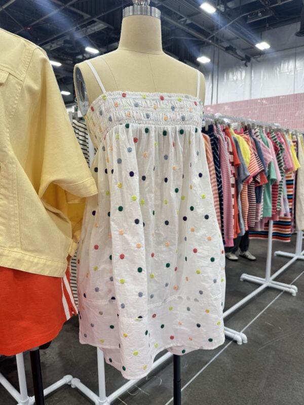 Photo of a mannequin wearing a white sundress with colorful embroidered polka dots and thin straps at a women’s fashion trade show.