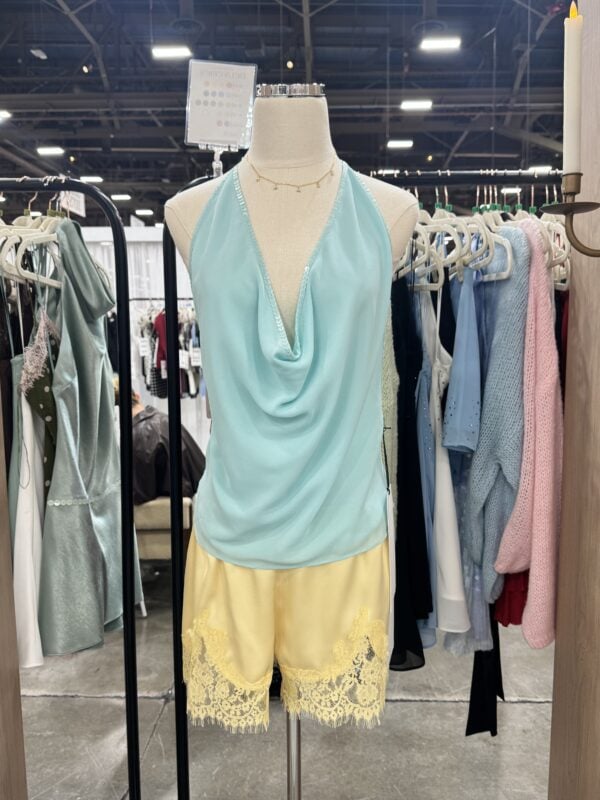 Photo of a mannequin wearing a light blue draped halter top with sequin trim and yellow lace-trimmed shorts at MAGIC 2026.